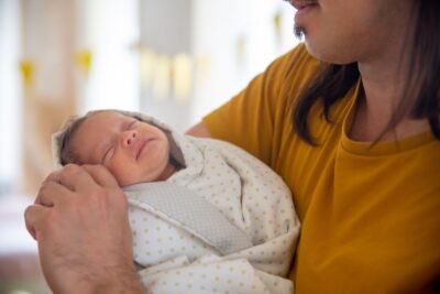 Un père tient son nouveau-né endormi à la maison pendant son congé supplémentaire de naissance